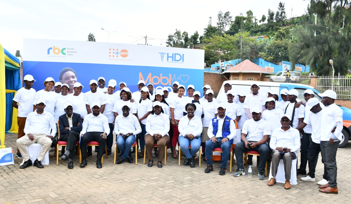 A group of Mobimentorship implementers sits in front of the HDI Mobi Mentorship banner wearing white shirts and white hats.